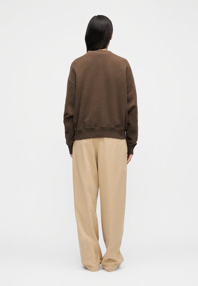Rjava jopa z ohlapnim krojem, rebrastimi manšetami in širokim pasom, kombinirana s svetlo bež, ohlapnimi hlačami.