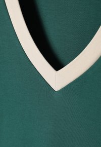 Green fabric with a smooth texture and a V-neck design, featuring a contrasting cream-colored trim along the neckline.