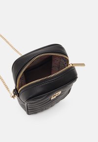 Czarna pikowana torebka z złotym zamkiem i łańcuszkowym paskiem, z wzorzystym wnętrzem oraz małym złotym akcentem z przodu.