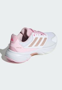 White athletic shoe featuring pink accents, mesh material, textured rubber sole, and three beige stripes on the side. Model name "COURTJAM."