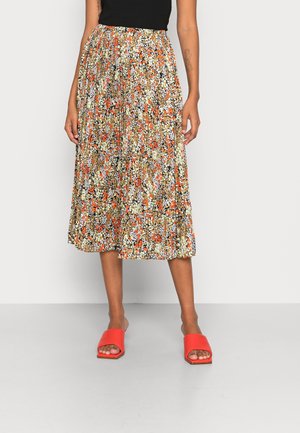 Femme portant une jupe midi plissée à motif floral orange, blanc et noir, un haut noir et des sandales slides à bout ouvert orange vif.