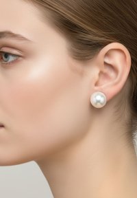 Orecchini a perno con perla dalla superficie liscia e lucida. Forma rotonda e colore crema, inseriti in un tono di pelle neutro. Design semplice.