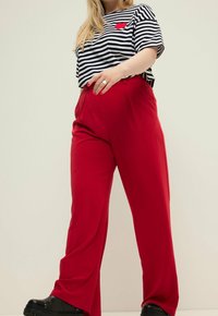 Czerwone spodnie o szerokich nogawkach w połączeniu z czarno-białą, pasiastą koszulką z krótkim rękawem, ozdobioną czerwoną aplikacją w kształcie serca. Gładka tkanina, luźny krój.