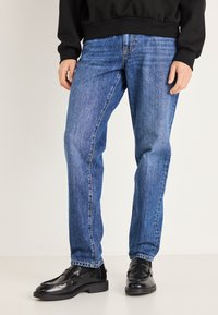 Vaqueros vaqueros azules con corte recto, con costuras de contraste y un diseño clásico de cinco bolsillos, combinados con mocasines negros de cuero.