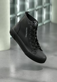 Μαύρα ψηλά αθλητικά παπούτσια κατασκευασμένα από λείο υλικό, με επίπεδη σόλα, κορδόνια μπροστά και λογότυπο "VALENTINO" στην εξωτερική πλευρά.