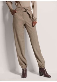 Lichtbruin taps toelopende broek met een hoge taille met riem, zijzakken en opgerolde enkels, gecombineerd met donkere haklaarzen.