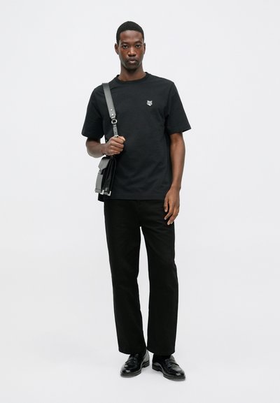 Tricou din bumbac negru cu mâneci scurte, logo mic pe piept, asociat cu pantaloni negri drepți și pantofi clasici din piele neagră. Geantă de umăr ajustabilă.