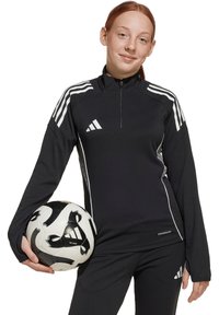 Zwarte sportieve lange mouwen top met ritssluiting bij de kraag, witte accenten en logo. Houdt een zwart-wit gestippelde voetbalsbal vast.