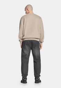 Beżowa bluza z długimi rękawami, okrągłym dekoltem i ściągaczem na dole, w połączeniu z luźnymi, ciemnoszarymi dżinsami i czarnymi trampkami.