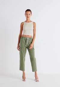Beige krátký top s přiléhavým střihem, spárovaný se zelenými cargo kalhotami s nastavitelnou šňůrkou a bočními kapsami. Modelka má na sobě stříbrné podpatky.