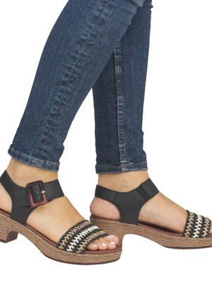 Black leather sandals with a woven strap featuring black and cream colors. Chunky, textured heel with a buckle detail on the ankle strap.
