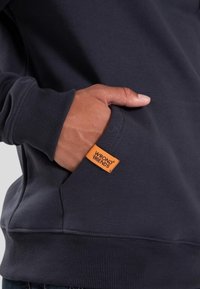 Marine sweatshirt met een kangoeroezak, voorzien van een oranje label. Gepolsterde ribbels aan de manchetten en tailleband. Zachte, zichtbare stofsamenstelling.