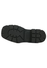 Suola in gomma nera con motivo di grip testurizzato, caratterizzata da scanalature e creste profonde per una migliore aderenza. Etichetta del marchio "GUESS" e taglia "38" in rilievo.