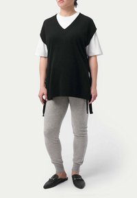 Svart, stickad ärmlös tröja med V-ringning, lagd över en vit skjorta. Matcher med ljusgråa sweatpants och svarta platta skor.