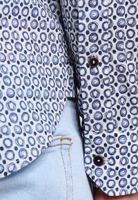 Kortärmad skjorta i lätt tyg, med ett blått och marinblått cirkulärt mönster. Inkluderar mörka knappar och är parat med ljusblått tyg.