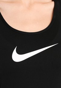 Black sleeveless top with a round neckline, featuring a prominent white Nike logo in the center. Smooth texture and stretchy fabric.