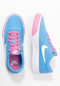 Blå skateboardskor i duk med rosa snören och detaljer, med en vit Nike-logotyp och en texturerad gummisula.