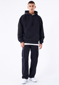 Svart hoodie med framficka, matchad med marinblå cargobyxor med två sidofickor; avslutad med vita sneakers.