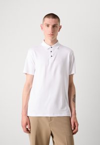 Witte polo met korte mouwen, voorzien van een knoopsluiting en een subtiel logo. Glad textuur en aansluitende pasvorm, gecombineerd met beige broek.