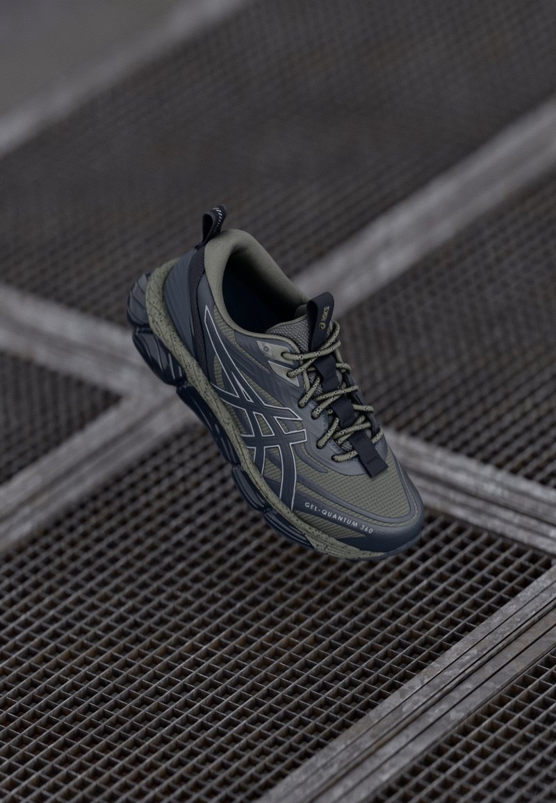 Baskets ASICS GEL-Quantum 360 gris et noir flottant au-dessus d'une surface métallique en grille avec une semelle texturée et un design à lacets.