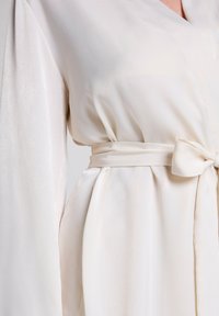 Silk robe in light cream with long sleeves. Features a belted waist tied in a bow, smooth texture, and subtle sheen.