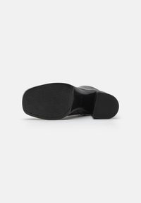 Suela de zapato de tacón alto negra con base de goma texturizada y agarre con patrón de diamante; cuenta con un leve tacón y borde liso.