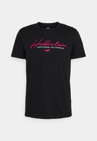 Svart bomull T-shirt med en rosa broderad "Hollister"-logotyp och texten "Southern California". Standard passform med rund hals.