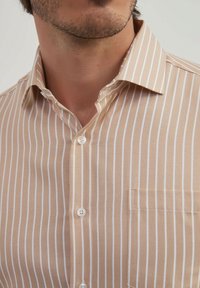 Chemise à manches longues rayée tan avec des rayures blanches verticales, une poche sur la poitrine et un col standard en tissu texturé.