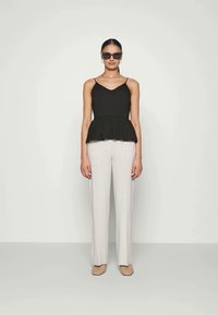 Svart peplum topp med tynne stropper, kombinert med lysegrå, tilpassede bukser. Modellen har svarte solbriller og beige, flettede slip-on sko.