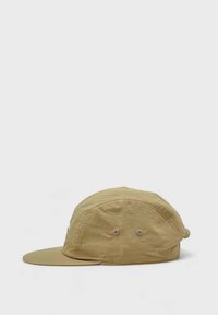 Beige lippalakki, jossa on kaareva lippa ja kevyt kangas. Sivuille on ommeltu kaksi ilmanvaihtoaukkoa, ja muotoilu on yksinkertainen.