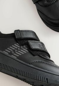 Schwarze Sneakers mit einer strukturierten Lederoberfläche, doppelten Velcro-Riemen, gerippten Außensohlen und einem diagonalen Streifenmuster mit Branding.
