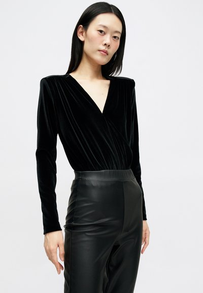 Body din catifea neagră, cu mâneci lungi, design cu decolteu adânc în V și talie strânsă, asociat cu pantaloni negri din piele ecologică cu talie înaltă.