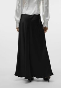 Zwarte, vloeiende maxi-rok gemaakt van soepele stof, met een brede zoom en een ontspannen pasvorm, gecombineerd met een witte blouse met lange mouwen.