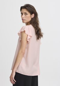 Helles rosa Bluse mit rüschierten Ärmeln, lockere Passform, aus weichem Stoff. Der Rücken hat einen runden Ausschnitt und dezente seitliche Schlitze.
