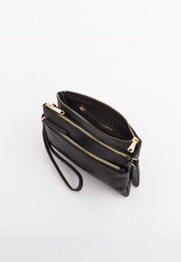 Sort lædertaske med tre lynlåscompartments, guldfarvede hardware-detaljer og et sidehåndledsstrop til bæring. Tekstureret overflade.