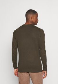 Maglione a maglia verde scuro con maniche lunghe, scollatura rotonda e polsini a costine, abbinato a pantaloni di velluto a coste marrone chiaro. Design minimalista.