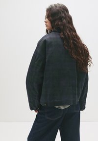 �Übergroße karierte Jacke in dunkelblau und grün, mit langen Ärmeln, geripptem Kragen und lockerer Passform, getragen über einem karierten Hemd.