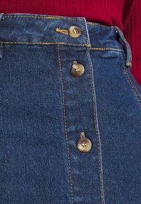 Falda vaquera de talle alto con cinco botones metálicos, costuras doradas en contraste y un acabado de tela lisa en azul oscuro.