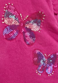 Tessuto fucsia con due farfalle ricamate in paillettes multicolori e accenti dorati, che mostrano motivi e texture intricati.