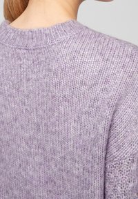 Liliowy sweter na drutach z prążkowanym dekoltem i fakturowaną tkaniną. Charakteryzuje się luźnymi ściegami i różnorodnymi odcieniami fioletu w wzorze dzianiny.