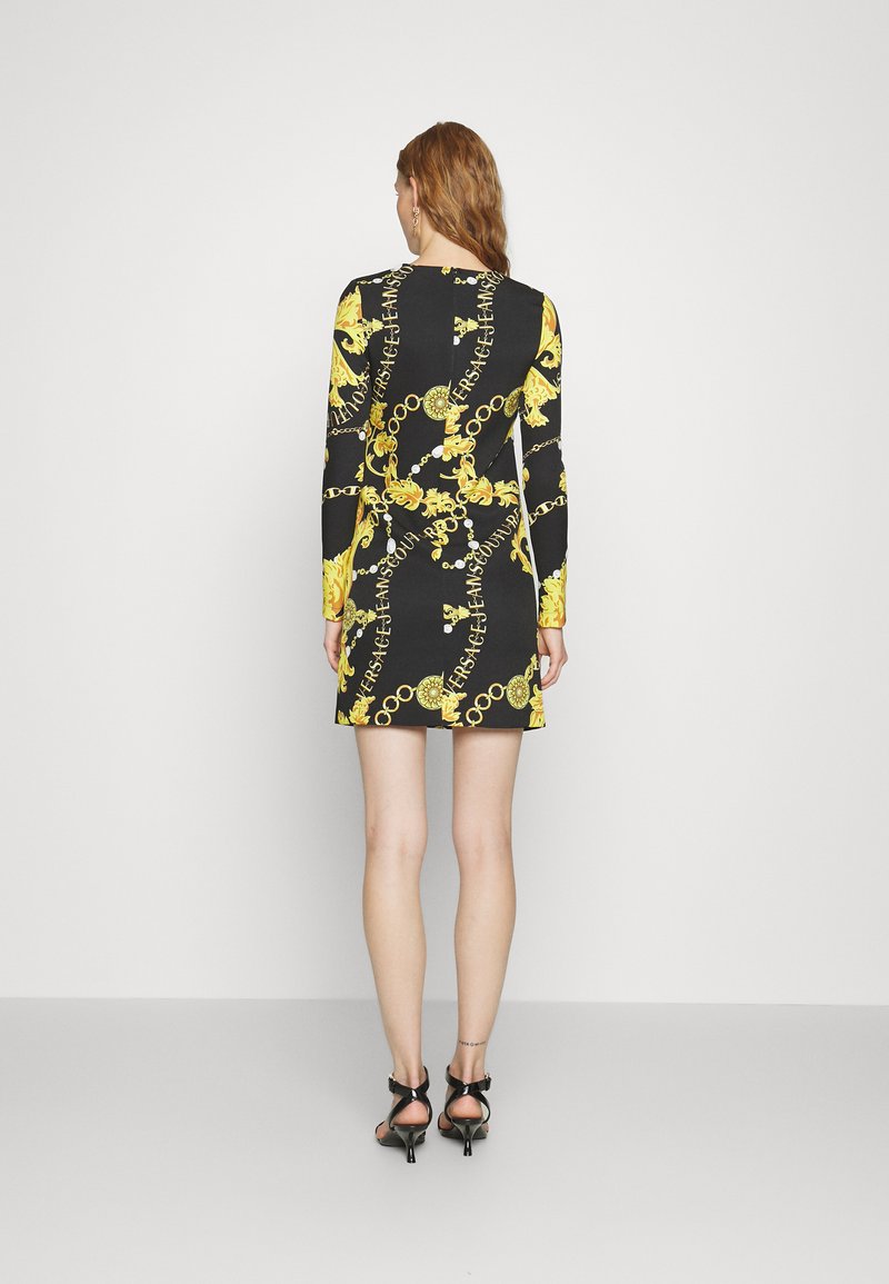 Vestito mini a maniche lunghe in nero con stampa barocca gialla e design a catena, caratterizzato da una silhouette attillata e una scollatura a metà schiena.