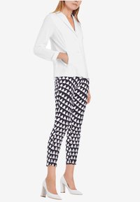 Witte blazer met dubbele knopen en notch-lapel, gecombineerd met zwarte broek met een geometrisch wit driehoekpatroon. Ivoor blokhak schoenen.