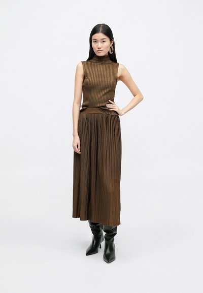 Brown ribbed knit sleeveless top paired with a matching long pleated skirt. Model wears knee-high black heeled boots.
