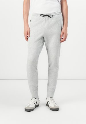 Light grey jogger pants with an elastic waistband and drawstring. Features side zip pockets and tapered legs. Worn with white sneakers.