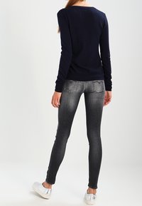 Suéter de punto navy, jeans de mezclilla gris ajustados y zapatillas plateadas. El suéter tiene mangas largas y escote en forma de barco; los jeans presentan bolsillos traseros y un acabado desgastado.