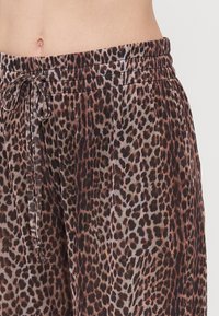 Leopard-print trousers in soft fabric, featuring an elastic waistband and drawstring closure. Colors include brown, black, and beige spots.