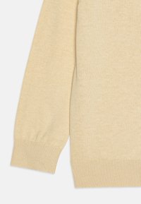 Beige strikkegenser med lange, litt puffete ermer og ribbede mansjetter. Stoffet har en jevn tekstur i en ensfarget nyanse.