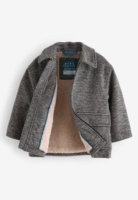 Manteau enfant gris et blanc à motif pied-de-poule avec doublure polaire beige et une fermeture éclair, partiellement ouvert pour montrer la texture intérieure douce.