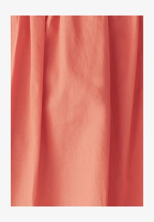 Breskve barve tkanina z gladko teksturo, ki vključuje mehko nabranje, kar ustvarja tekoč videz.