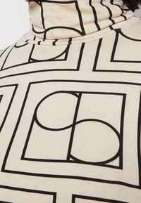 Maglione a collo alto in tessuto crema con un audace motivo geometrico nero di quadrati e cerchi, con un design aderente e texture a costine.